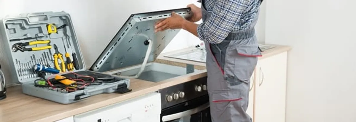 Cooktop repair technician lifting a built-in stovetop for service in Kansas City, MO