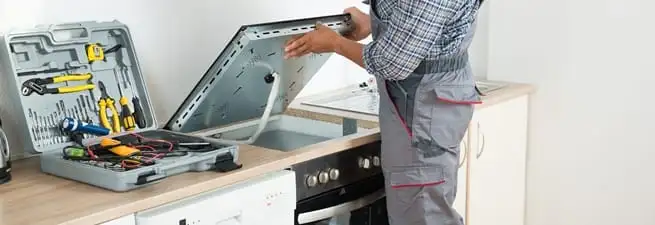 Cooktop repair technician lifting a built-in stovetop for service in Kansas City, MO