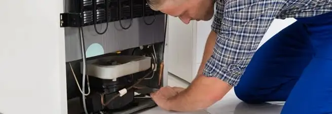 Refrigerator repair technician servicing the compressor and condenser area in Kansas City, MO