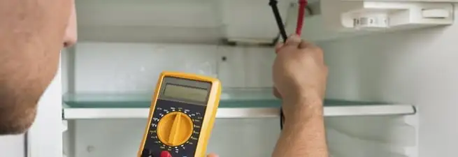 Refrigerator repair technician testing electrical components with a multimeter in Kansas City, MO