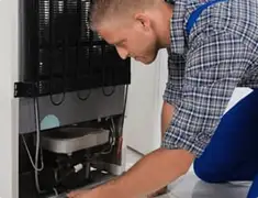 Refrigerator repair technician servicing the compressor and condenser area in Kansas City, MO