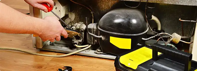 Refrigerator repair technician fixing the compressor and wiring in Kansas City, MO